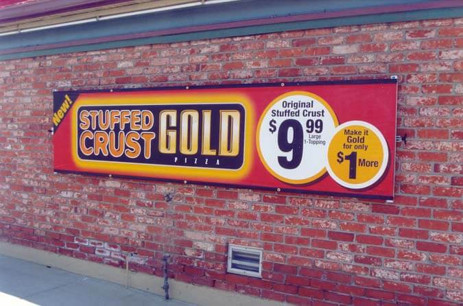 Mounted outdoor banner on brick wall for stuffed crust gold pizza